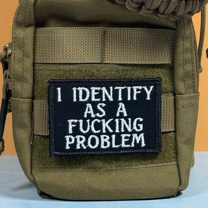 An olive green tactical pouch with a black rectangular patch featuring white embroidered text that reads 'I IDENTIFY AS A FUCKING PROBLEM'.