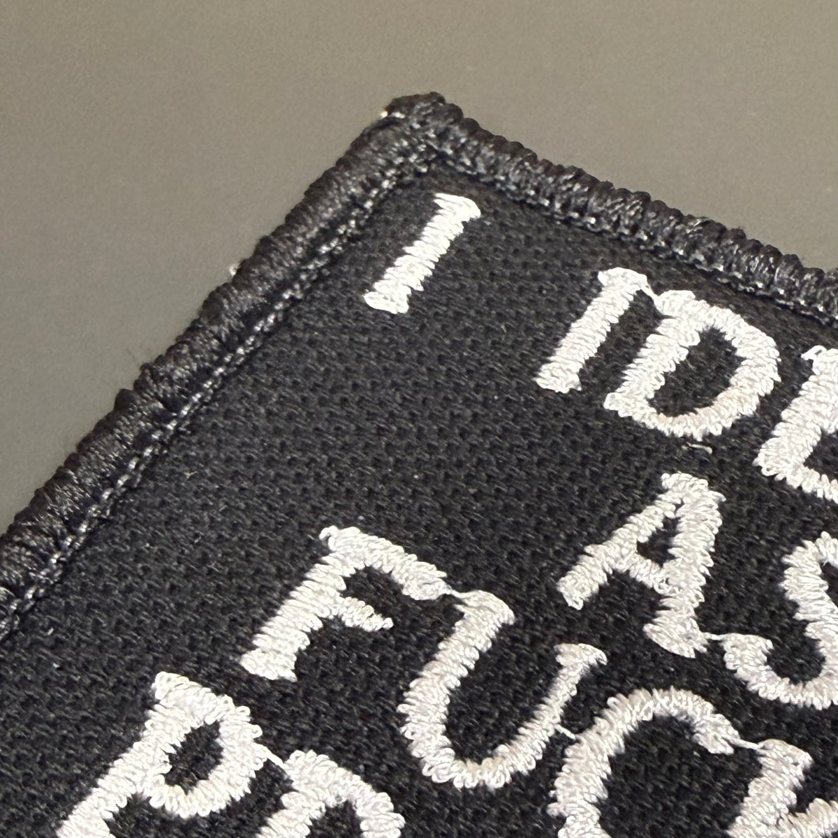 Close-up of a black embroidered patch with white text reading 'I DID AS FUCK' on a neutral gray background.