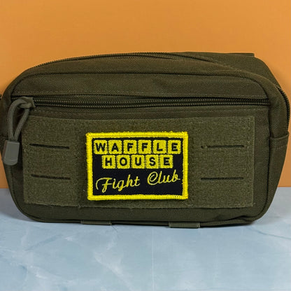 An olive green tactical pouch with a front zippered pocket and a prominent embroidered patch reading 'WAFFLE HOUSE Fight Club' in yellow and black, set against an orange background.