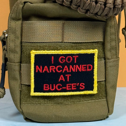 An olive green tactical pouch featuring a rectangular embroidered patch with a black background, red text reading 'I GOT NARCANNED AT BUC-EE'S', and a yellow border.
