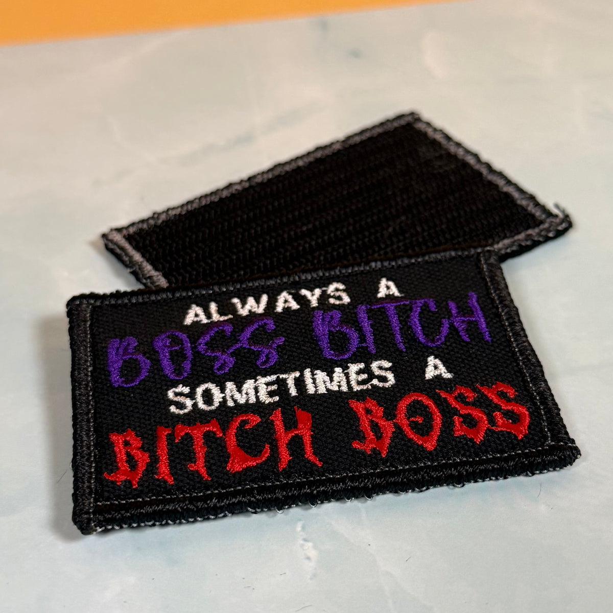 Two embroidered rectangular patches with a black background and humorous text. The front patch reads 'ALWAYS A BOSS BITCH SOMETIMES A BITCH BOSS' in white, purple, and red lettering, with a black border.