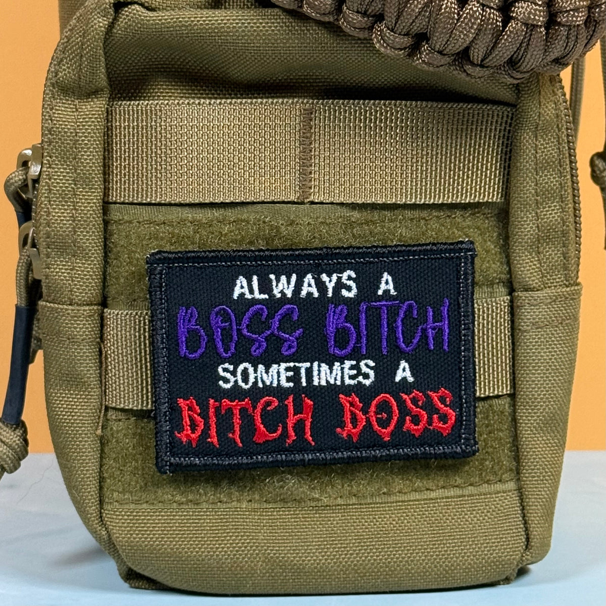 An olive green tactical pouch featuring a black embroidered patch with the text 'ALWAYS A BOSS BITCH SOMETIMES A BITCH BOSS' in white, purple, and red lettering.