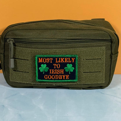 An olive green tactical pouch with a front zippered pocket and a rectangular embroidered patch that reads 'MOST LIKELY TO IRISH GOODBYE' in orange text with green shamrocks, set against an orange and light blue background.