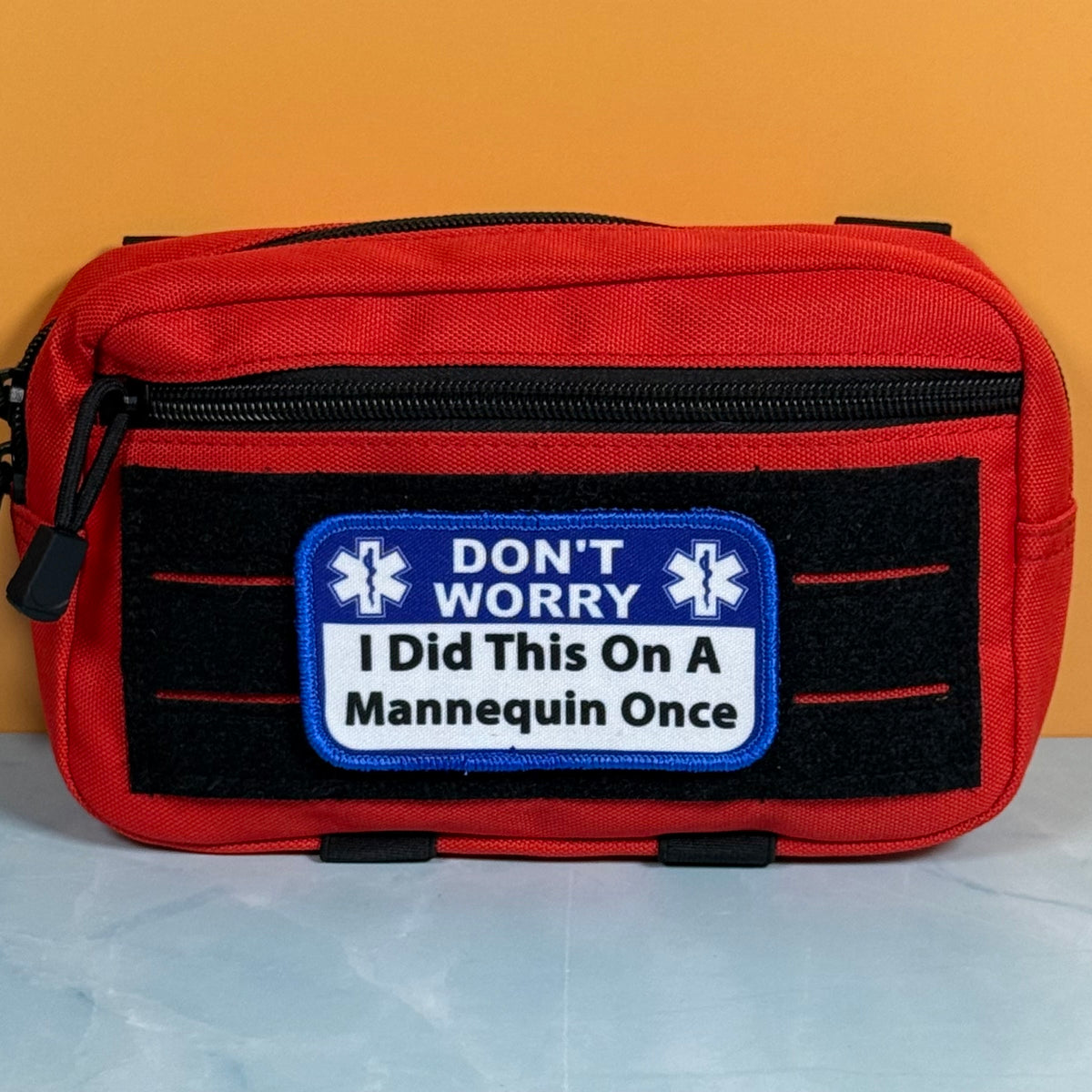 I Did This On a Mannequin Once printed canvas morale patch, a red and black medical first aid pouch with a humorous patch that the design letteringT WORRY I Did This On A Mannequin Once' on a yellow and white background.