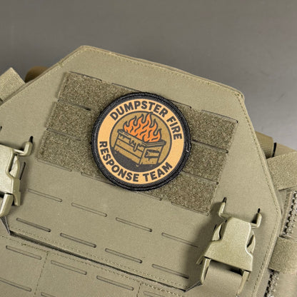 A circular embroidered patch reading 'DUMPSTER FIRE RESPONSE TEAM' with a burning dumpster graphic, attached to tan tactical webbing on a matching tan vest or bag.