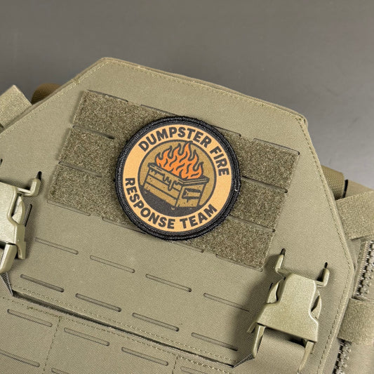 A circular embroidered patch reading 'DUMPSTER FIRE RESPONSE TEAM' with a burning dumpster graphic, attached to tan tactical webbing on a matching tan vest or bag.