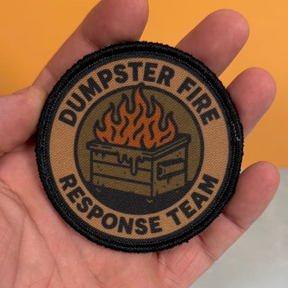 A round embroidered patch reading 'DUMPSTER FIRE RESPONSE TEAM' with a fire graphic in the center, held in a person's hand against an orange background.