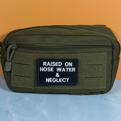 Raised on Hose Water & Neglect embroidered morale patch: olive green tactical pouch with a black embroidered patch that reads 'RAISED ON HOSE WATER & NEGLECT' in white text, set against a split orange and light blue background.