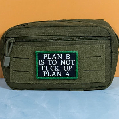 An olive green tactical pouch with a front zipper and a rectangular embroidered patch that reads 'PLAN B IS TO NOT FUCK UP PLAN A' in white text on a black background with a green border, set against an orange and blue background.