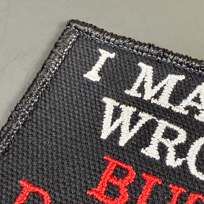 Close-up of a black embroidered patch with white and red text reading 'I MAKE WRO...' on a gray background.