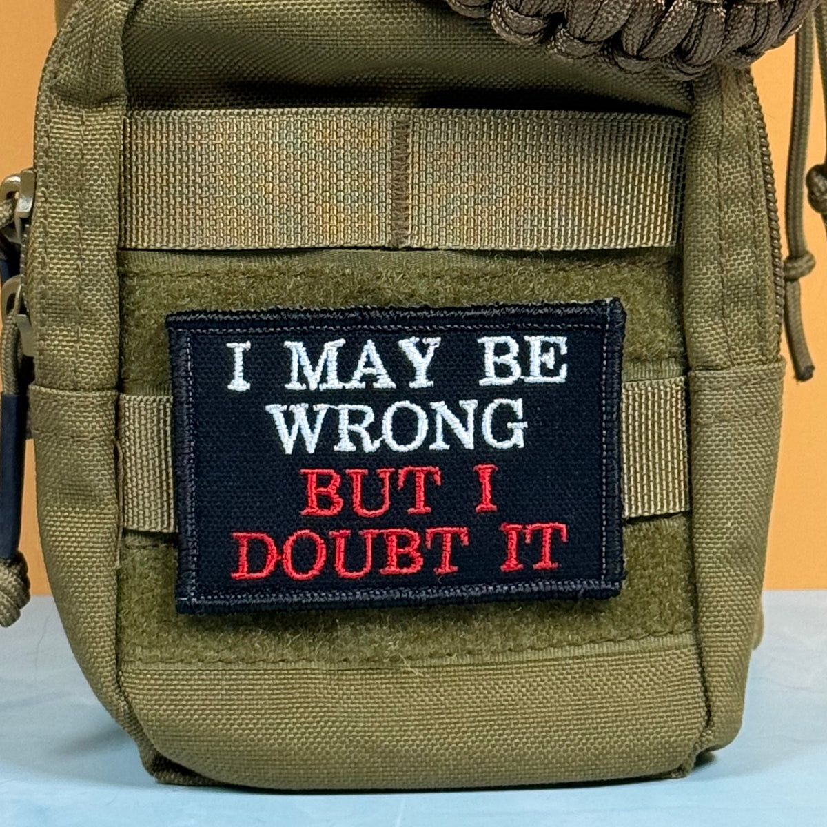 An olive green tactical pouch with a black embroidered patch that reads 'I MAY BE WRONG BUT I DOUBT IT' in white and red text.
