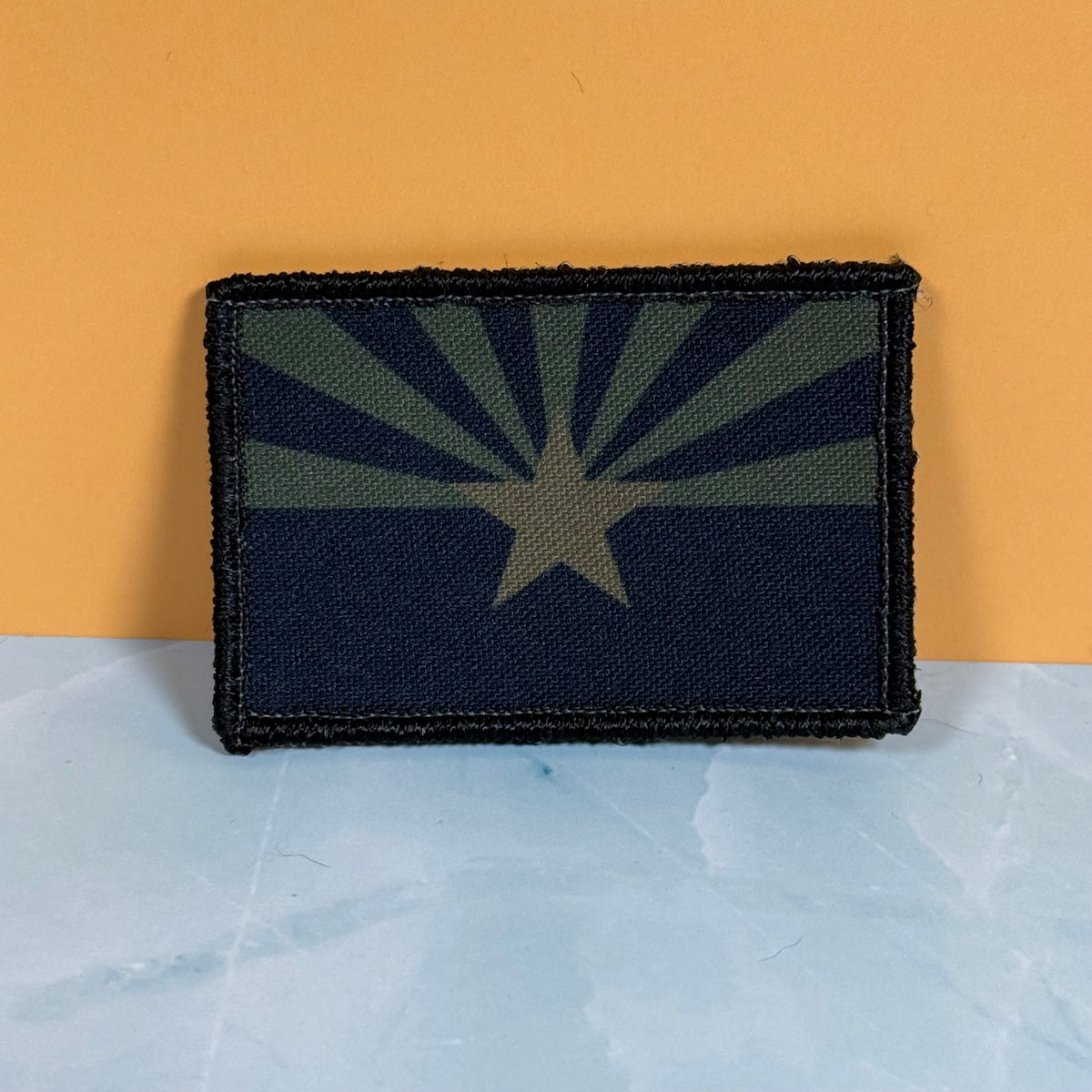 Arizona State Flag printed canvas morale patch featuring the Arizona state flag in a dark camouflage pattern, set against a split orange and light blue background.