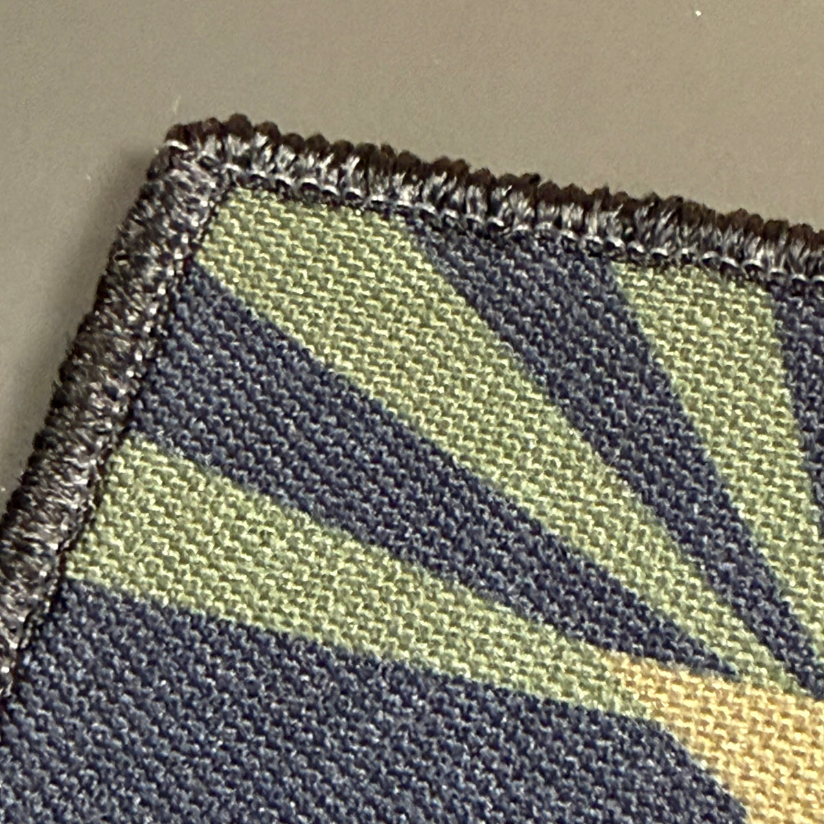 Arizona State Flag printed canvas morale patch, close-up of a woven fabric patch with a geometric sunburst pattern in olive green, dark navy, and tan, finished with a dark stitched border.