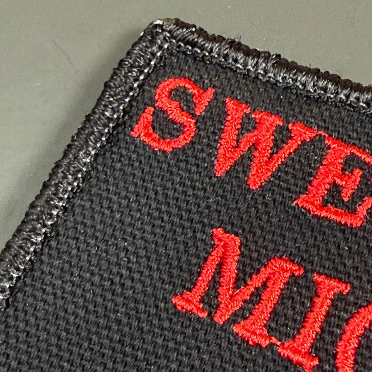 Close-up of a black embroidered patch with red lettering reading 'SWEET M...'.