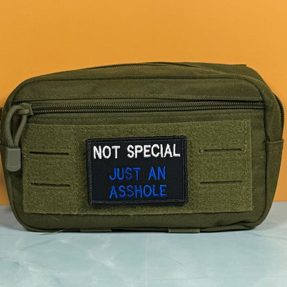 An olive green tactical pouch with a front zipper and a black embroidered patch that reads 'NOT SPECIAL JUST AN ASSHOLE' in white and blue text, set against a solid orange background.