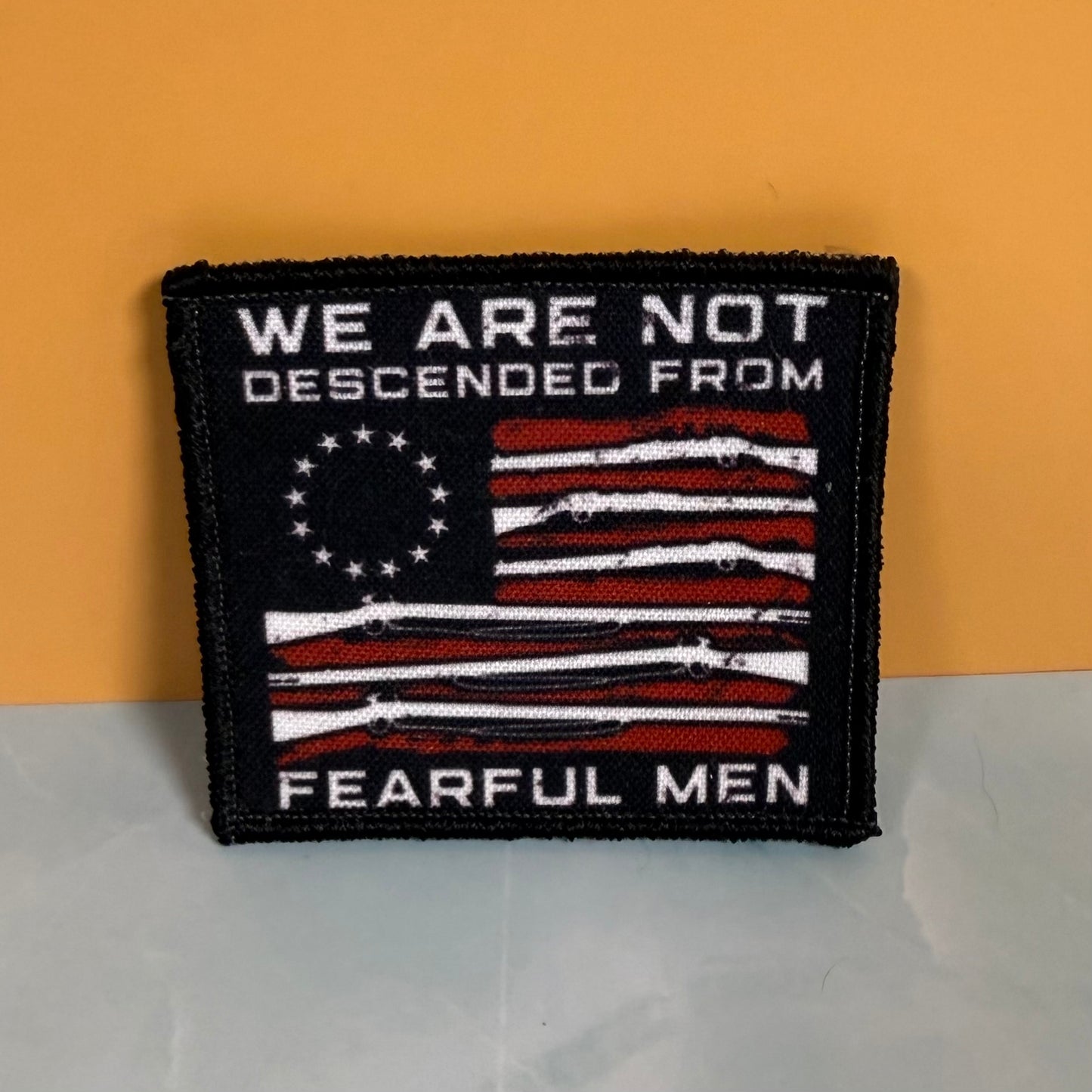 A square embroidered patch with a black border, featuring a distressed American flag design in red, white, and black, with the text 'WE ARE NOT DESCENDED FROM FEARFUL MEN' in white on a black background.