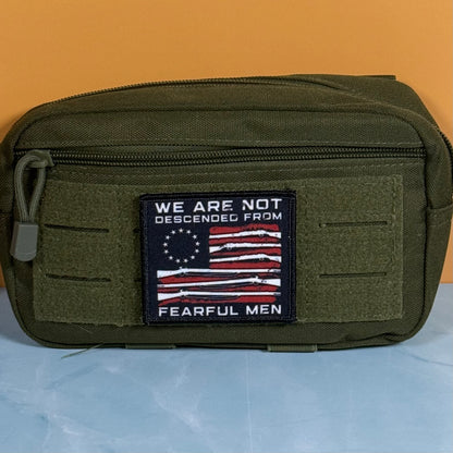 An olive green tactical pouch with a front zipper and a rectangular embroidered patch featuring a stylized American flag and the text 'WE ARE NOT DESCENDED FROM FEARFUL MEN'.