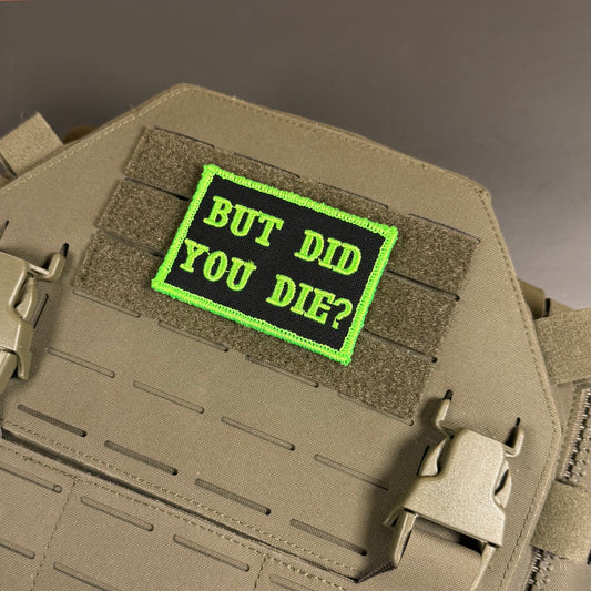 But Did You Die embroidered morale patch: tactical patch with the text 'BUT DID YOU DIE?' in bright green on a black background, shown attached to tan MOLLE webbing on a tactical vest or plate carrier.