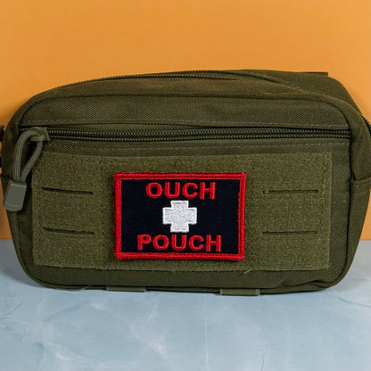 An olive green tactical pouch with a front zipper and a custom embroidered patch reading 'OUCH POUCH' with a white cross on a black background and red border, set against an orange background.