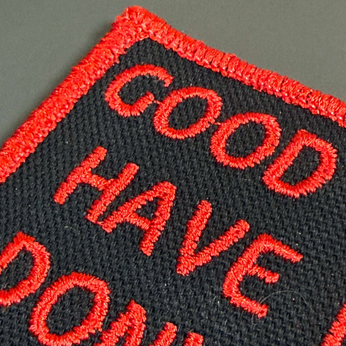 Close-up of an embroidered patch with red text reading 'GOOD HAVE DO...' on a black background with a red stitched border.