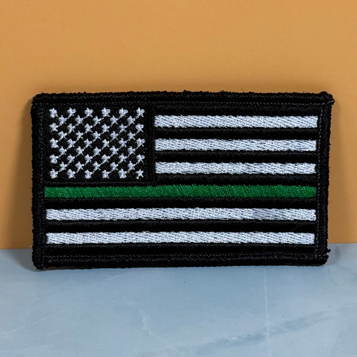 Thin Green Line Tactical American Flag embroidered morale patch: of a black and white American flag with a single green stripe, representing a 'Thin Green Line' design, displayed against a solid orange background.