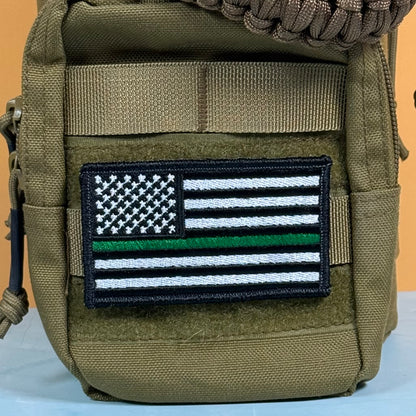 Thin Green Line Tactical American Flag embroidered morale patch: olive drab tactical pouch featuring a 'Thin Green Line' American flag embroidered patch on the front, with a brown paracord strap visible at the top.