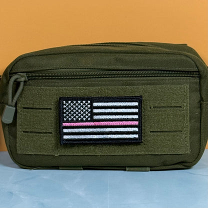 Breast Cancer Awareness Thin Pink Line American Flag embroidered morale patch: olive green tactical pouch with a front zippered pocket and a rectangular embroidered American flag patch featuring a single pink stripe, shown against an orange.