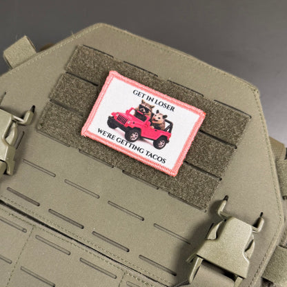 Get In Loser We're Getting Tacos printed canvas morale patch, dog in a red jeep, the design letteringRE GETTING TACOS', attached to olive drab tactical webbing on a matching olive drab bag.