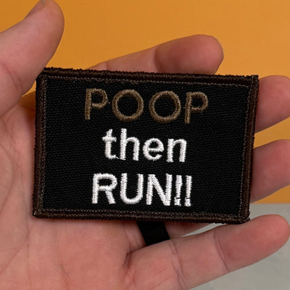 A hand holding a rectangular black embroidered patch with the text 'POOP then RUN!!' in brown and white lettering, set against a solid orange background.