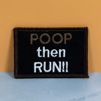 A rectangular embroidered patch with the text 'POOP then RUN!!' on a black background, placed against a warm orange wall and a light blue-gray surface.