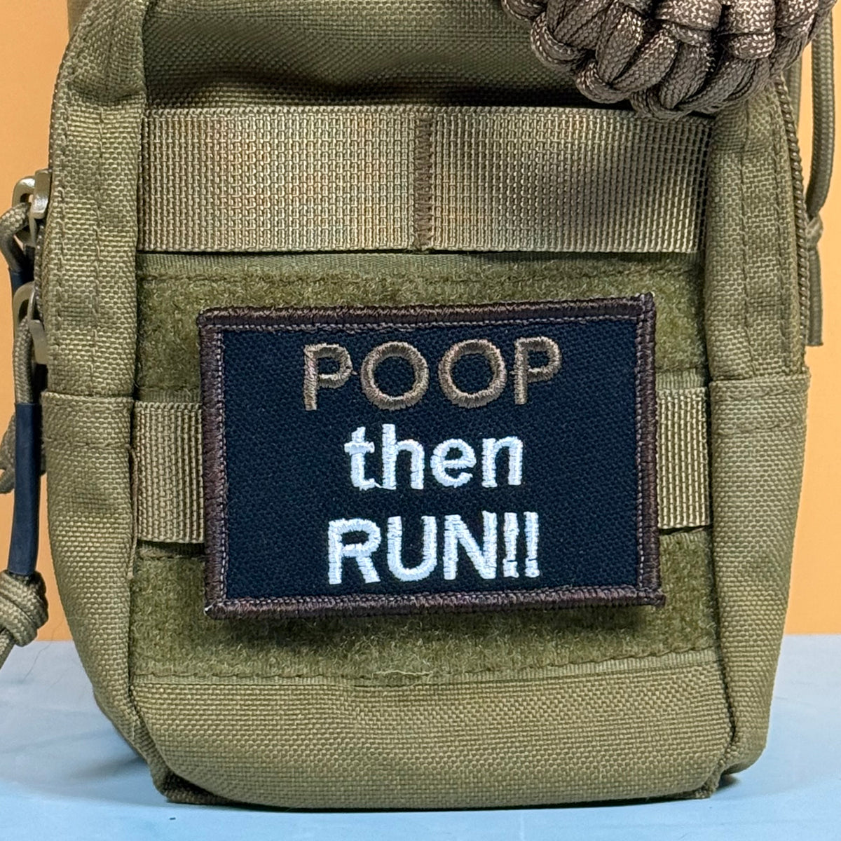 An olive green tactical pouch with a dark navy embroidered patch that reads 'POOP then RUN!!' in white and tan lettering, shown against a simple orange and blue background.