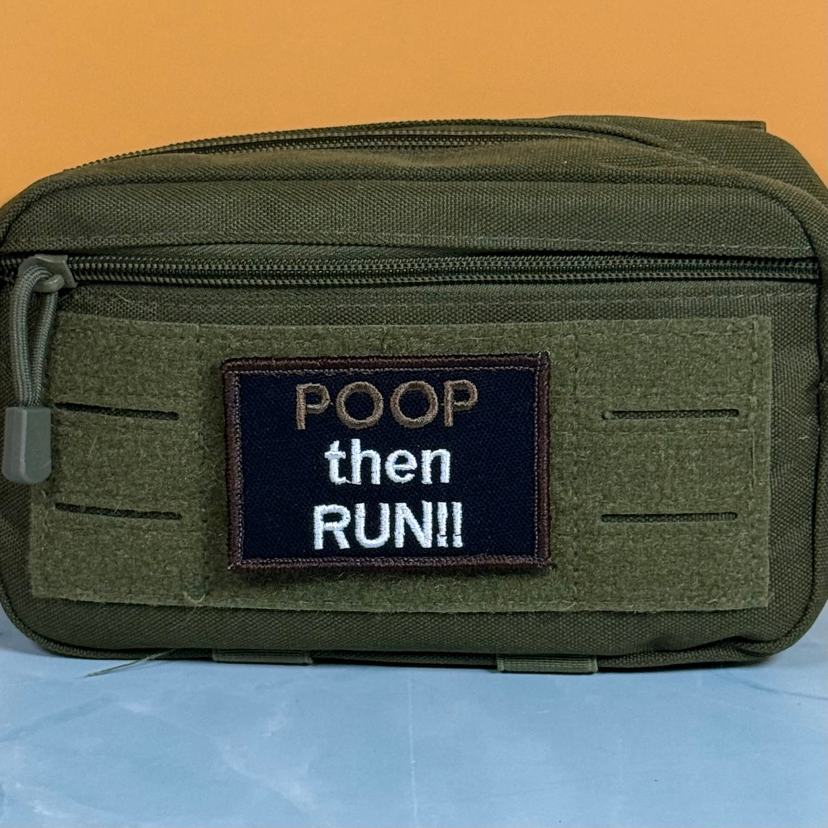An olive green tactical pouch with a front hook-and-loop patch that reads 'POOP then RUN!!' in white and tan lettering, set against a solid orange background.