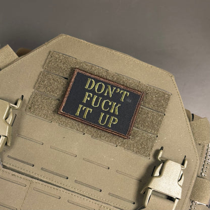 A rectangular embroidered patch with the text 'DON'T FUCK IT UP' in yellow on a black background, sewn onto a tan tactical vest with Velcro and quick-release buckles.