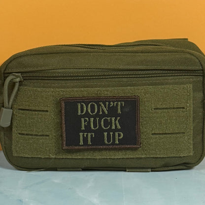 An olive green tactical pouch with a black rectangular patch on the front that reads 'DON'T FUCK IT UP' in tan lettering, set against a solid orange background.