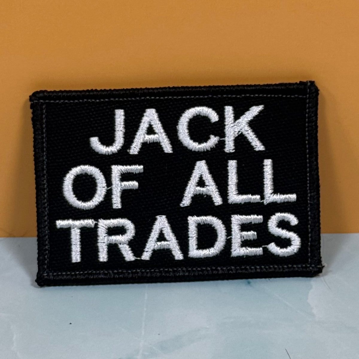 Jack Of All Trades embroidered morale patch: black embroidered patch with white text reading 'JACK OF ALL TRADES' on a two-tone background.