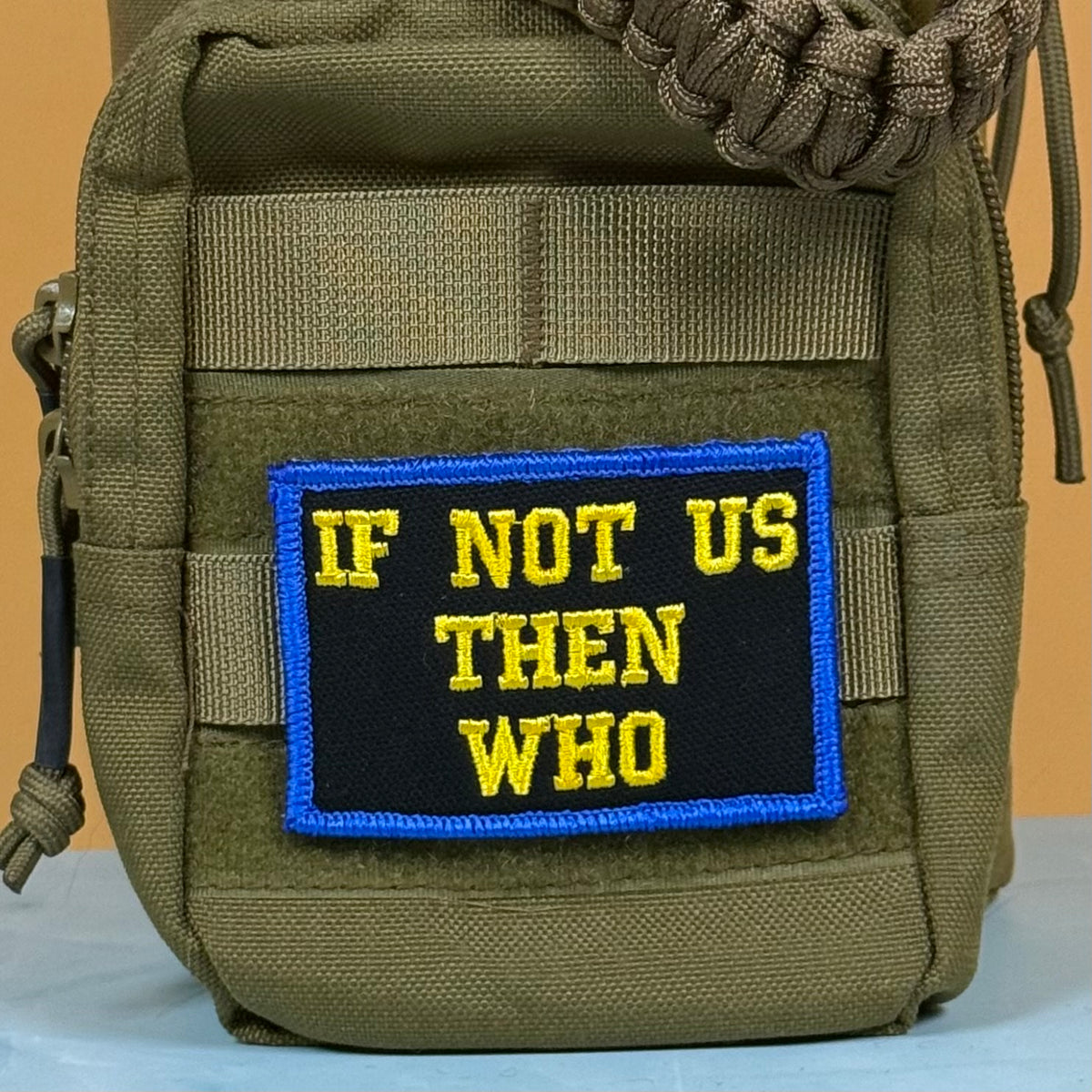 If Not Us Then Who embroidered morale patch: olive green tactical pouch featuring a rectangular embroidered patch with the text 'IF NOT US THEN WHO' in yellow on a black background with a blue border.