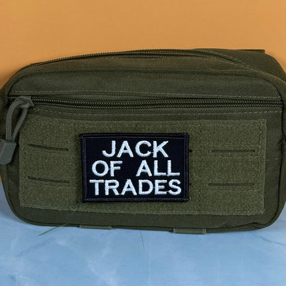 Jack Of All Trades embroidered morale patch: olive green tactical pouch with a black rectangular patch featuring the white embroidered text 'JACK OF ALL TRADES', set against a split orange and light blue background.
