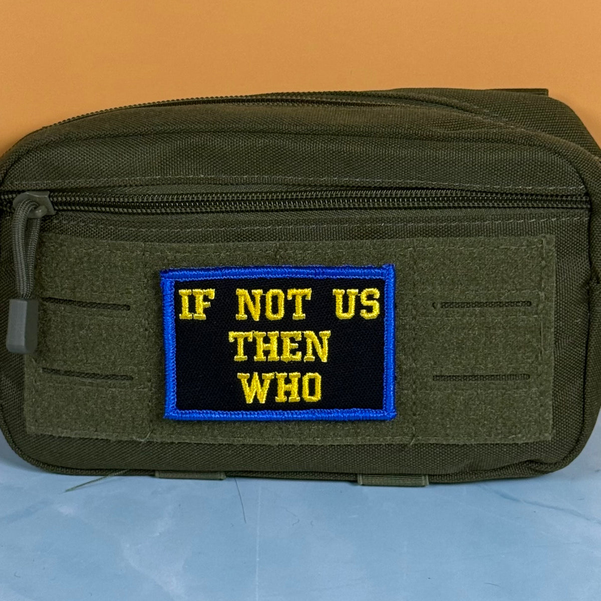 If Not Us Then Who embroidered morale patch: olive drab tactical pouch with a rectangular embroidered patch that reads 'IF NOT US THEN WHO' in yellow text on a black background with a blue border, set against a split orange and blue.