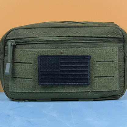 Blackout No Quarters Given American Flag embroidered morale patch: olive drab tactical pouch with a front zipper and a black embroidered American flag patch on a hook-and-loop panel, set against a split orange and blue background.