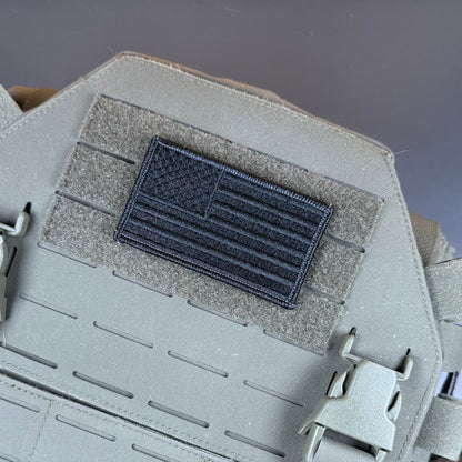 Blackout No Quarters Given American Flag embroidered morale patch: dark gray embroidered American flag patch mounted on a gray tactical vest with hook-and-loop fastening, shown in a close-up product detail shot.