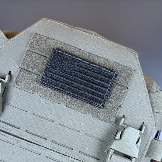 A dark gray embroidered American flag patch mounted on a gray tactical vest with hook-and-loop fastening, shown in a close-up product detail shot.