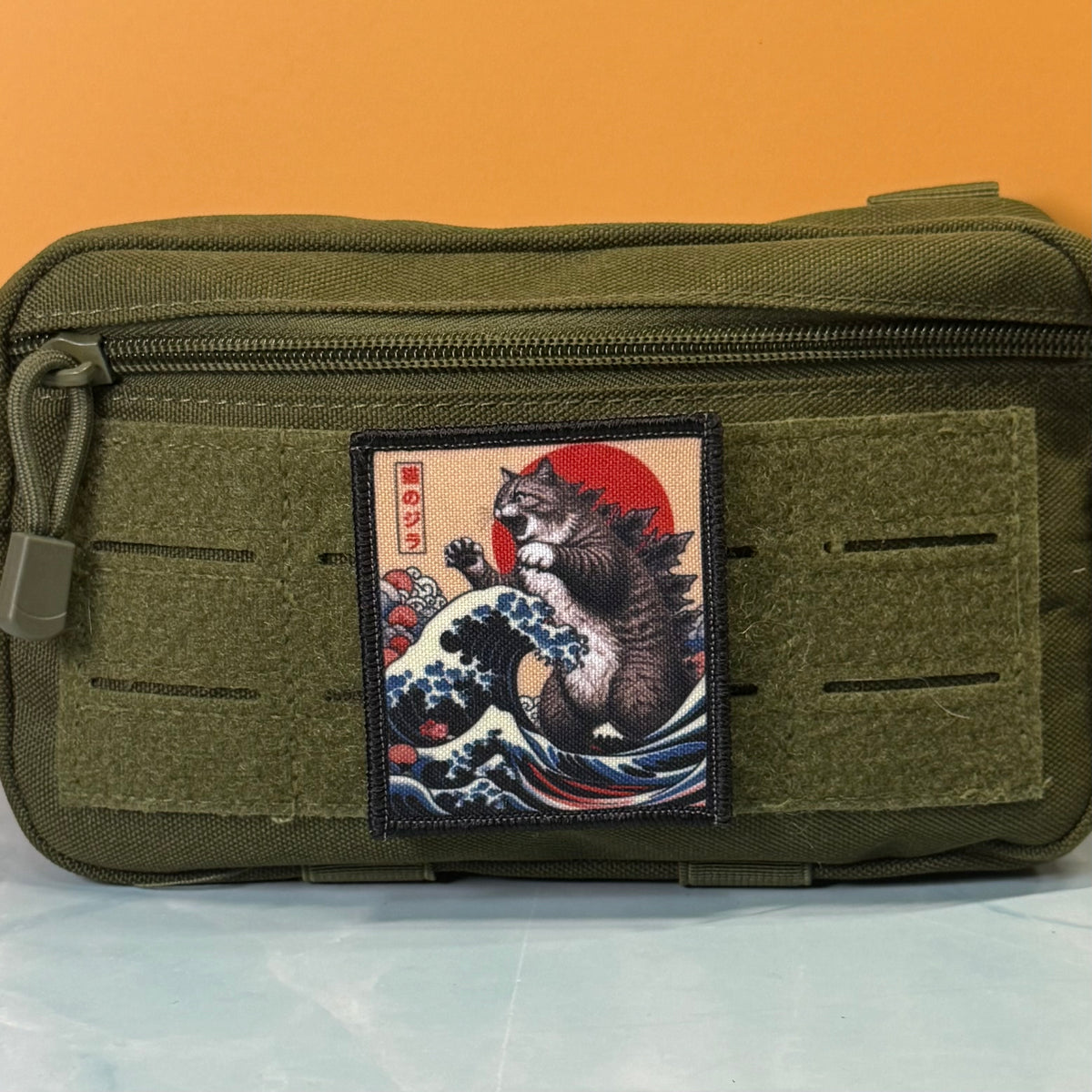 Catzilla printed canvas morale patch, an olive green tactical pouch featuring a rectangular printed patch with a Japanese ukiyo-e style cat riding a wave under a red sun.