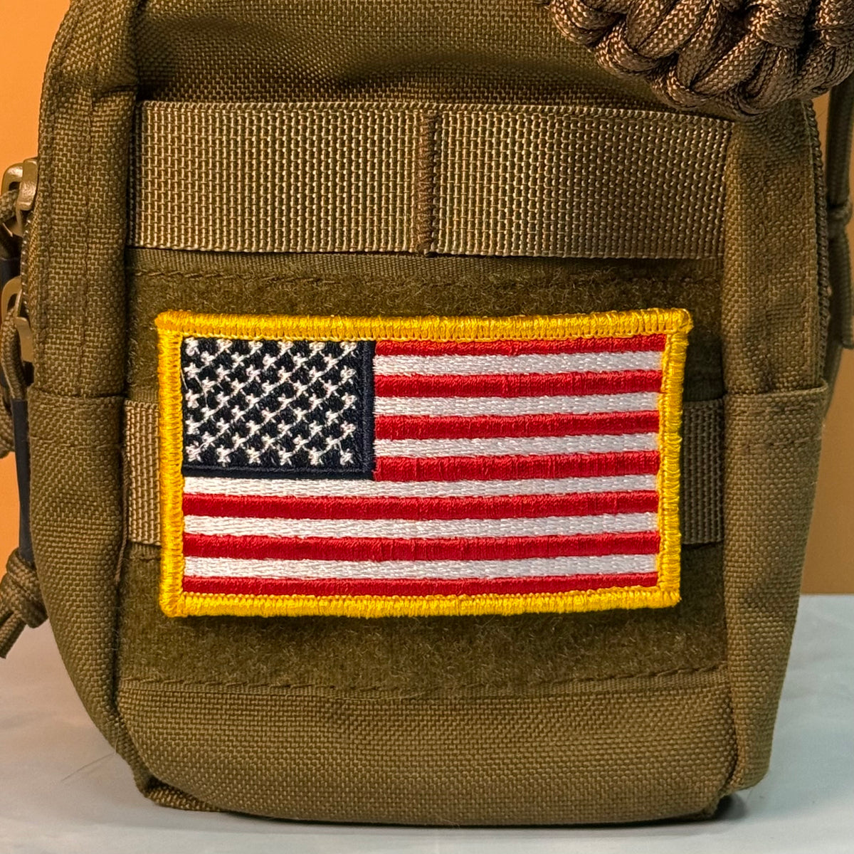 American Flag embroidered morale patch: United States flag patch with a yellow border, applied to the front pocket of an olive drab tactical bag.