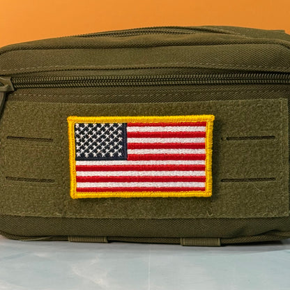 American Flag embroidered morale patch: olive drab tactical pouch with a rectangular embroidered American flag patch on the front, set against a solid orange background.