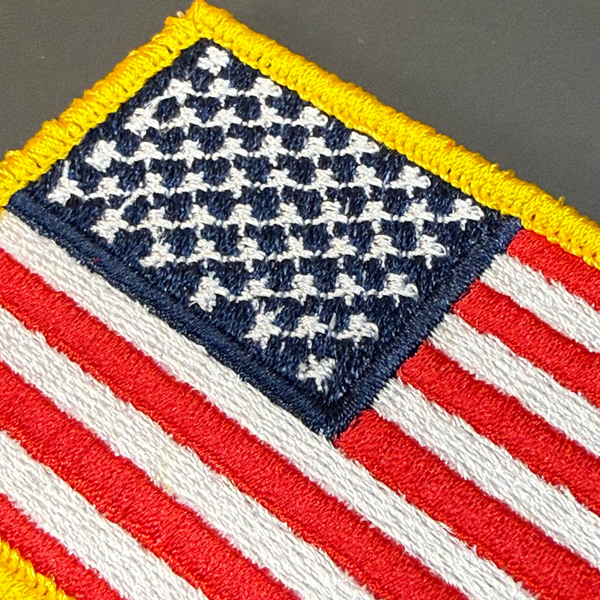 American Flag embroidered morale patch: embroidered American flag patch with red and white stripes, a blue canton with white stars, and a yellow border on a dark gray background.
