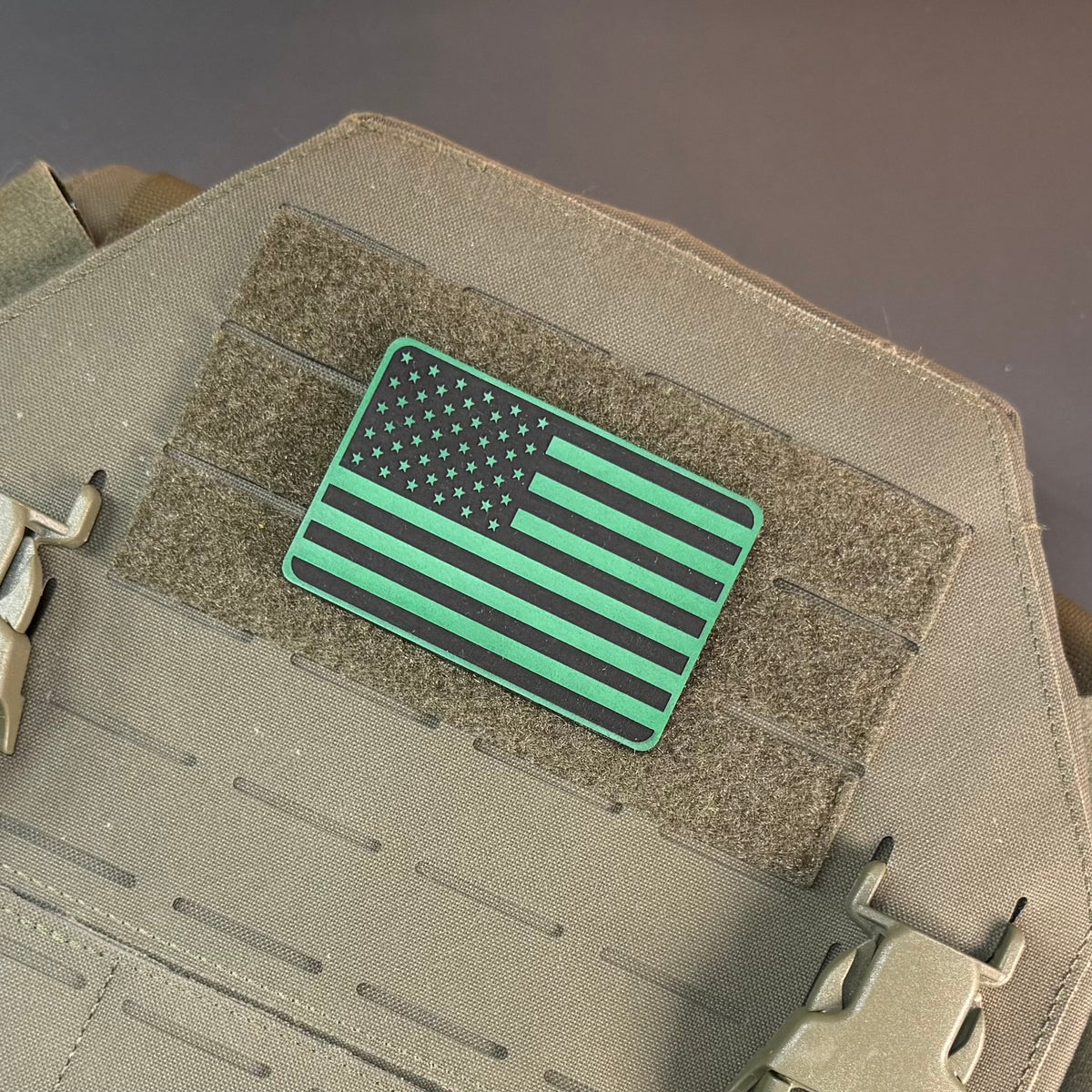 Tactical Synthetic Engraved American laser-engraved synthetic morale patch: a rectangular tactical patch featuring a stylized American flag design in black and bright green, mounted on a tan tactical vest with hook-and-loop fastening.