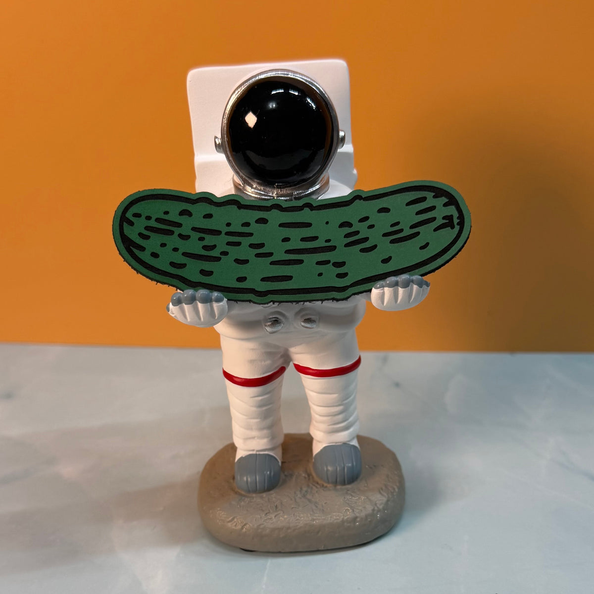 Dill Pickle laser-engraved synthetic morale patch: a novelty figurine of an astronaut holding a large green pickle, standing on a gray base against an orange background.