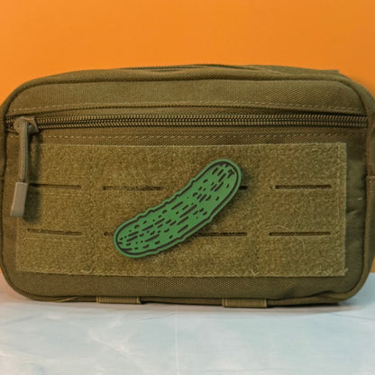 Dill Pickle laser-engraved synthetic morale patch: an olive green tactical pouch with a front hook-and-loop panel and a green cucumber-shaped patch, set against an orange background.