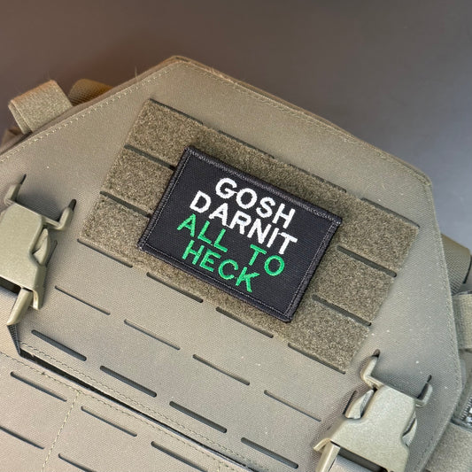 Gosh Darnit All To Heck, Polite Swearing embroidered morale patch: black embroidered patch with the phrase 'GOSH DARNIT ALL TO HECK' in white and green lettering, shown attached to a tan tactical vest or plate carrier.