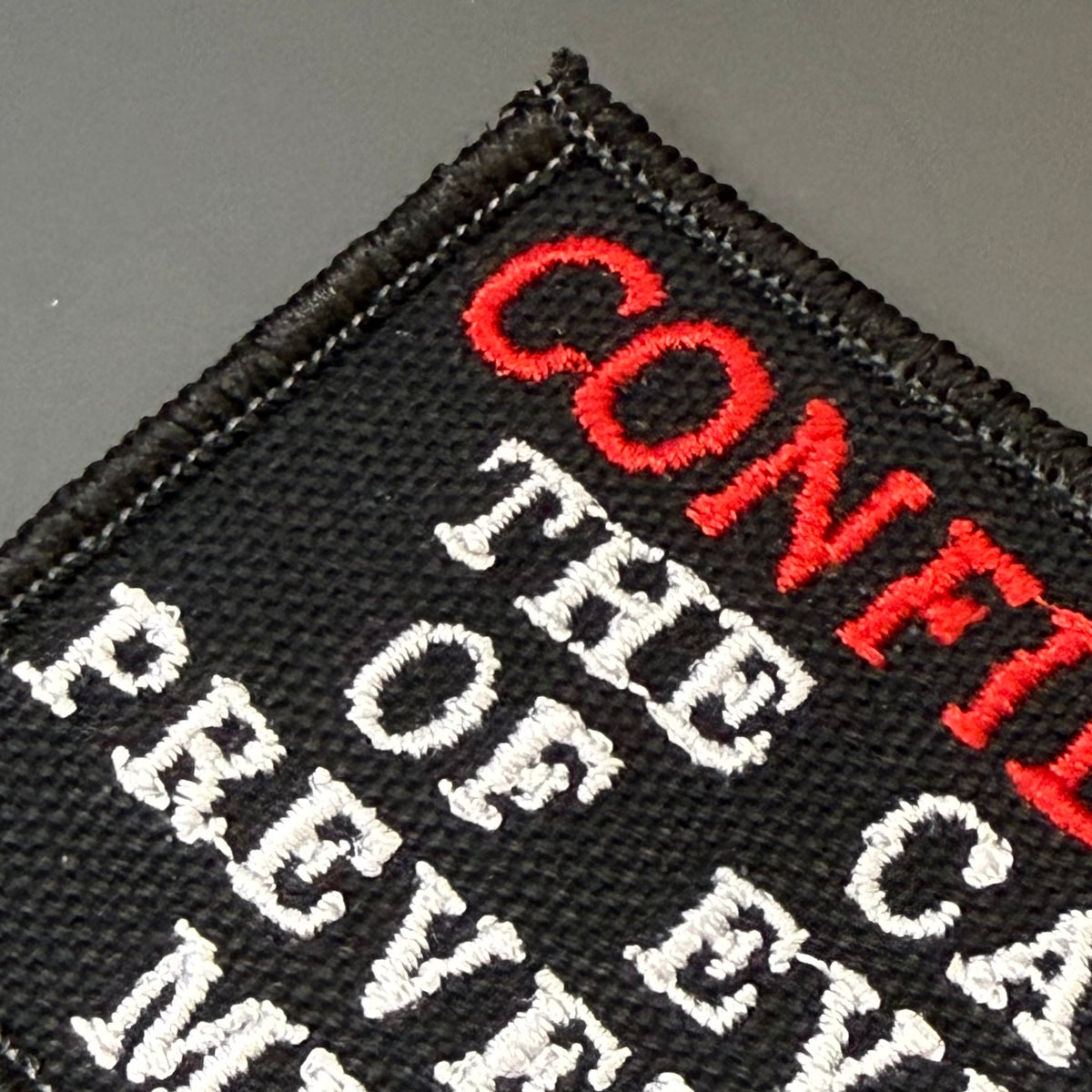Confidence Causes Mistakes embroidered morale patch: black embroidered patch with white and red text reading 'CONFIDENCE THE CARE OF EVOLVING' on a dark gray background.